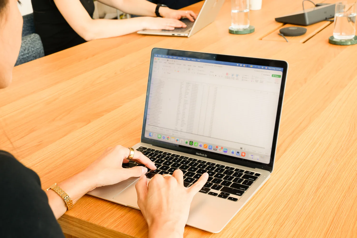 Two colleagues working on laptops at a shared desk, laptop screen blurred
