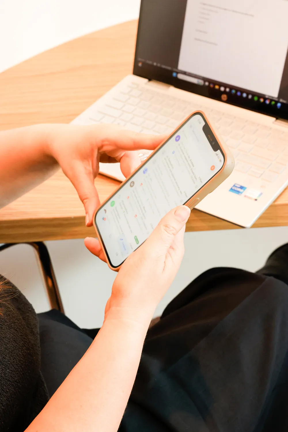 Person holding a phone showing a blurred inbox, laptop on the desk behind